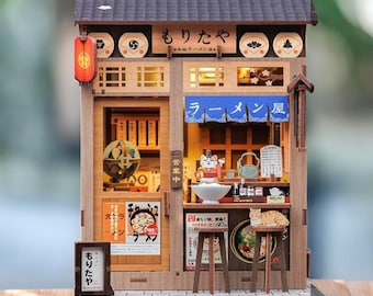 May include: A detailed miniature wooden Japanese ramen shop model with a dark grey roof, a red lantern, and Japanese signage. The shop includes a cat figurine and miniature food items, showcasing intricate craftsmanship.