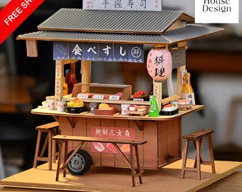 May include: A wooden model kit of a Japanese food stall with a red and white sign that says "Sushi" in Japanese. The stall has a wooden roof and a counter with a variety of sushi and other Japanese food items. The stall is on a wooden base with a brown background.