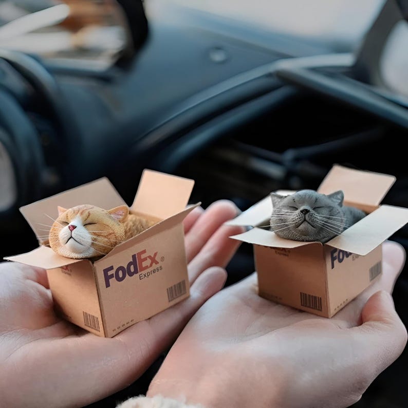 May include: Two small cardboard boxes with sleeping cats inside. The boxes are brown and have the FedEx logo printed on them. The cat in the left box is orange and white, and the cat in the right box is gray.