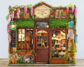 May include: A miniature dollhouse shop with a brown wooden facade, adorned with pink flowers and green foliage. The sign reads "Once Upon a Time... DOLLHOUSE SHOP". The shop features lit windows and a welcoming door.