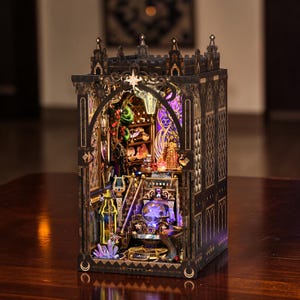 May include: A detailed, illuminated wooden model of a gothic-style building. The interior features miniature furniture, staircases, and decorative elements, with a warm, inviting glow from the internal lighting. The exterior is dark brown with intricate cut-out designs.