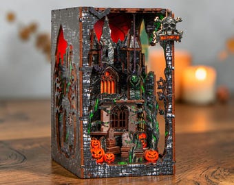 May include: A rectangular wooden Halloween diorama featuring a dark castle with glowing orange windows, a graveyard with tombstones, and carved pumpkins. The structure includes a skull and crossbones sign with the text HALLOWEEN.