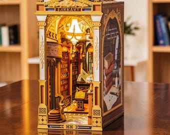 May include: A wooden book nook kit featuring a miniature library interior with a glowing chandelier, detailed bookshelves, a curved staircase, and a printed side panel showing a stack of books and a quill. The structure is labeled with the word LIBRARY.