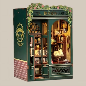 May include: A miniature wooden model of a bookstore with a green exterior and a sign that reads "Owl Bookstore". The store has a window display with books and a small owl figurine. The model is detailed with brickwork, vines, and a wooden door.