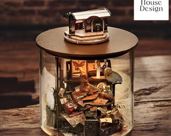 May include: A glass jar with a wooden lid and a miniature house on top. Inside the jar is a miniature scene with a desk, books, owls, and other objects. The jar is on a wooden surface. Pocket House Design.