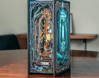 May include: A rectangular book nook insert featuring a multi-layered, laser-cut forest scene with a stone staircase leading to a gothic archway. The side panel displays intricate teal and gold filigree borders with the text 'THE GATE OF NO RETURN'.