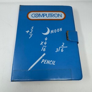 May include: A blue rectangular notebook with a magnetic closure flap. The cover features the text COMPUTRON in an orange oval, along with white printed graphics including math equations, a crescent moon, the word MOON, and a pencil with the word PENCIL.