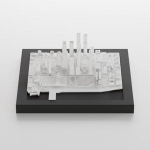 May include: A white 3D printed model of a city skyline, displayed on a black base. The model features tall buildings and a detailed cityscape.