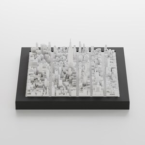 Pu&ograve; includere: Un modello 3D bianco di uno skyline cittadino, che include grattacieli ed edifici, &egrave; esposto in una cornice nera. Il modello &egrave; realizzato con piccoli cubi bianchi disposti in un reticolo.