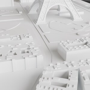 K&ouml;nnte beinhalten: Ein wei&szlig;es 3D-Modell einer Stadt mit einem Miniatur-Eiffelturm im Hintergrund. Das Modell besteht aus kleinen, rechteckigen Bl&ouml;cken, die Geb&auml;ude darstellen. Das Modell steht auf einer wei&szlig;en Oberfl&auml;che.