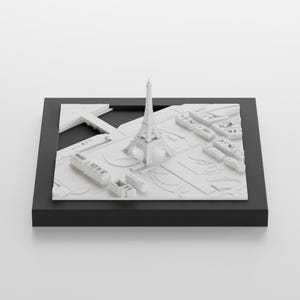 K&ouml;nnte beinhalten: Ein wei&szlig;es 3D-Modell des Eiffelturms und der umliegenden Pariser Stadtlandschaft, auf einem schwarzen Sockel pr&auml;sentiert.