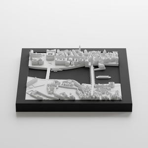 Puede incluir: Un modelo 3D blanco de una ciudad con edificios, calles y un r&iacute;o. El modelo est&aacute; colocado en un marco negro.