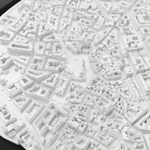 May include: A detailed, white 3D model of a city, showcasing buildings, streets, and urban planning. The model is a monochromatic representation of an urban landscape, with a high level of detail in the architectural structures.