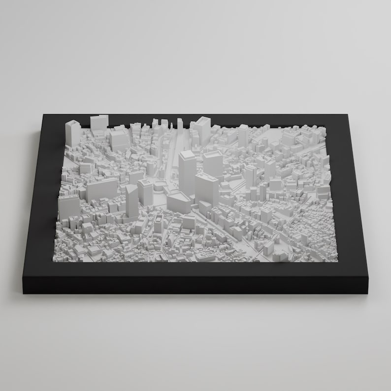 May include: A white 3D model of a city skyline in a black frame. The model is made of small, white blocks that represent buildings. The model is set against a white background.
