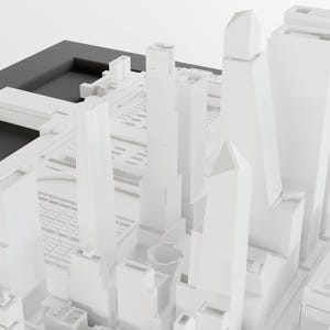 May include: A white model of a city skyline with tall buildings and a black base.