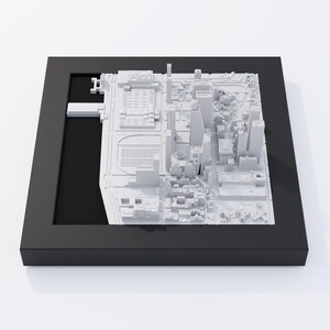 May include: A white 3D model of a city skyline, displayed in a black frame. The model is detailed and includes buildings, streets, and a waterfront.