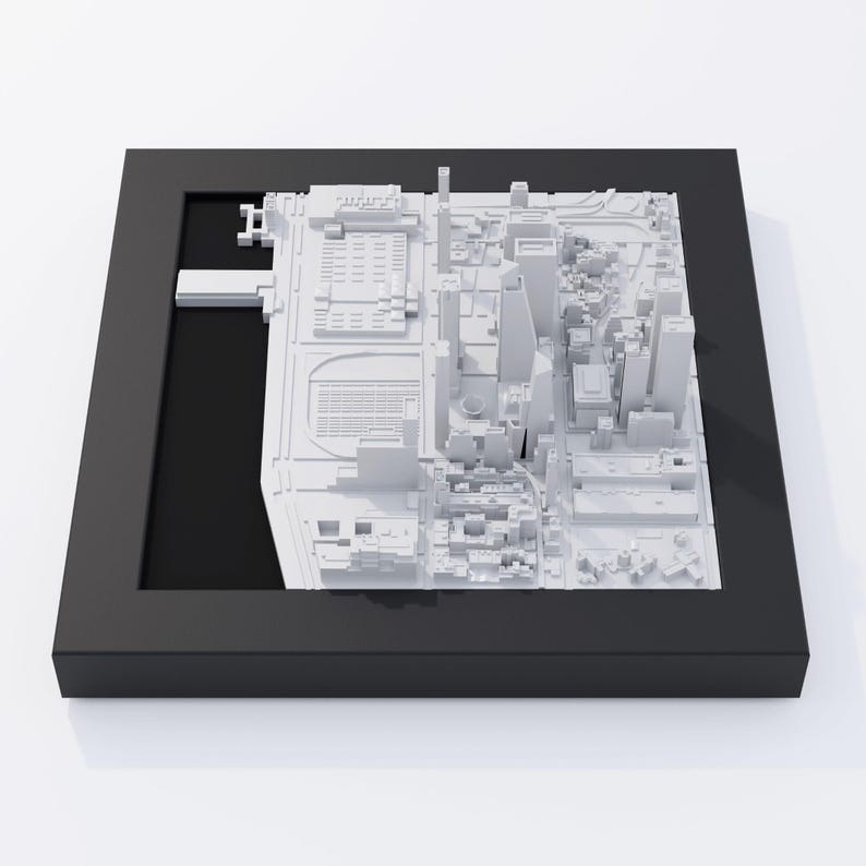 May include: A white 3D model of a city skyline, displayed in a black frame. The model is detailed and includes buildings, streets, and a waterfront.