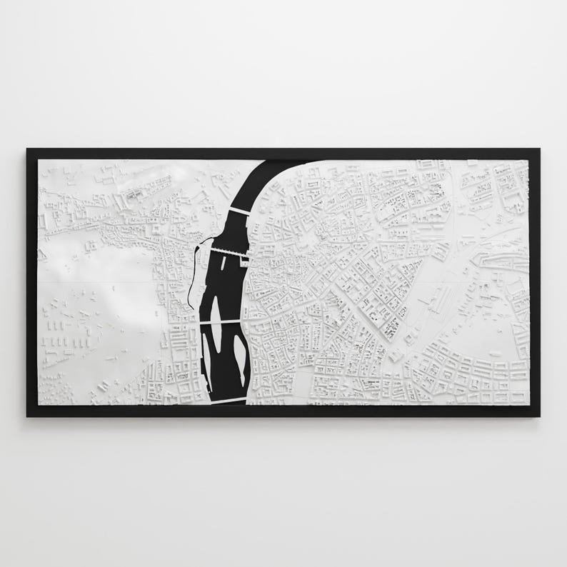 May include: A framed, three-dimensional white map with a black river running through it. The map is highly detailed, showing streets and buildings. The frame is black, and the overall aesthetic is modern and minimalist.