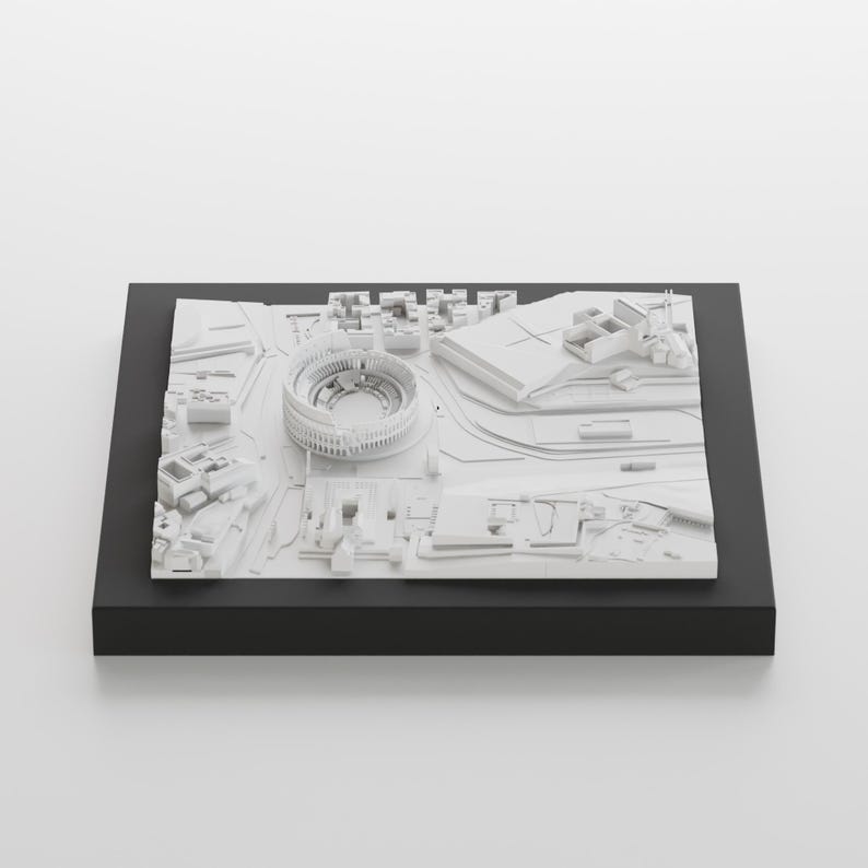 Puede incluir: Un modelo 3D blanco de una ciudad con un gran estadio en el centro. El modelo est&aacute; sobre una base negra.
