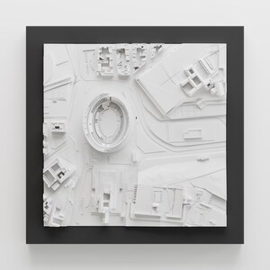 Puede incluir: Un modelo 3D blanco de una ciudad con un estadio en el centro. El modelo est&aacute; enmarcado en un marco negro.