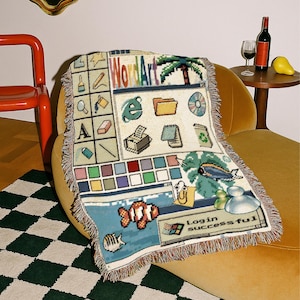 Peut inclure: Un plaid tiss&eacute; pr&eacute;sentant un design d'interface d'ordinateur des ann&eacute;es 90. Le motif inclut des ic&ocirc;nes de dossiers, une imprimante, un CD, un palmier, un poisson-clown et un trombone, avec le texte "WordArt" et "Login successful" imprim&eacute;.