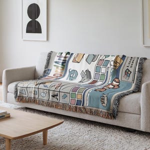 Peut inclure: Un plaid tiss&eacute; pr&eacute;sentant un design d'interface de bureau d'ordinateur des ann&eacute;es 90. Le motif comprend des ic&ocirc;nes pix&eacute;lis&eacute;es, une grille de carr&eacute;s color&eacute;s, un squelette de poisson et des &eacute;l&eacute;ments textuels comme WordArt et un logo style Windows.