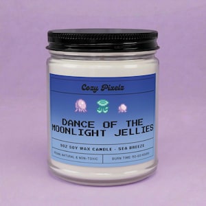 May include: A glass jar candle with a black lid and a blue label. The label reads "Cozy Pixelz" and "DANCE OF THE MOONLIGHT JELLIES". The candle is 9 oz soy wax, sea breeze scented, vegan, natural, and non-toxic, with a burn time of 50-60 hours.