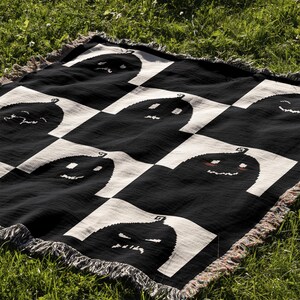 May include: Black and white checkered throw blanket with a pattern of smiling and frowning pumpkins. The blanket has a fringe border.