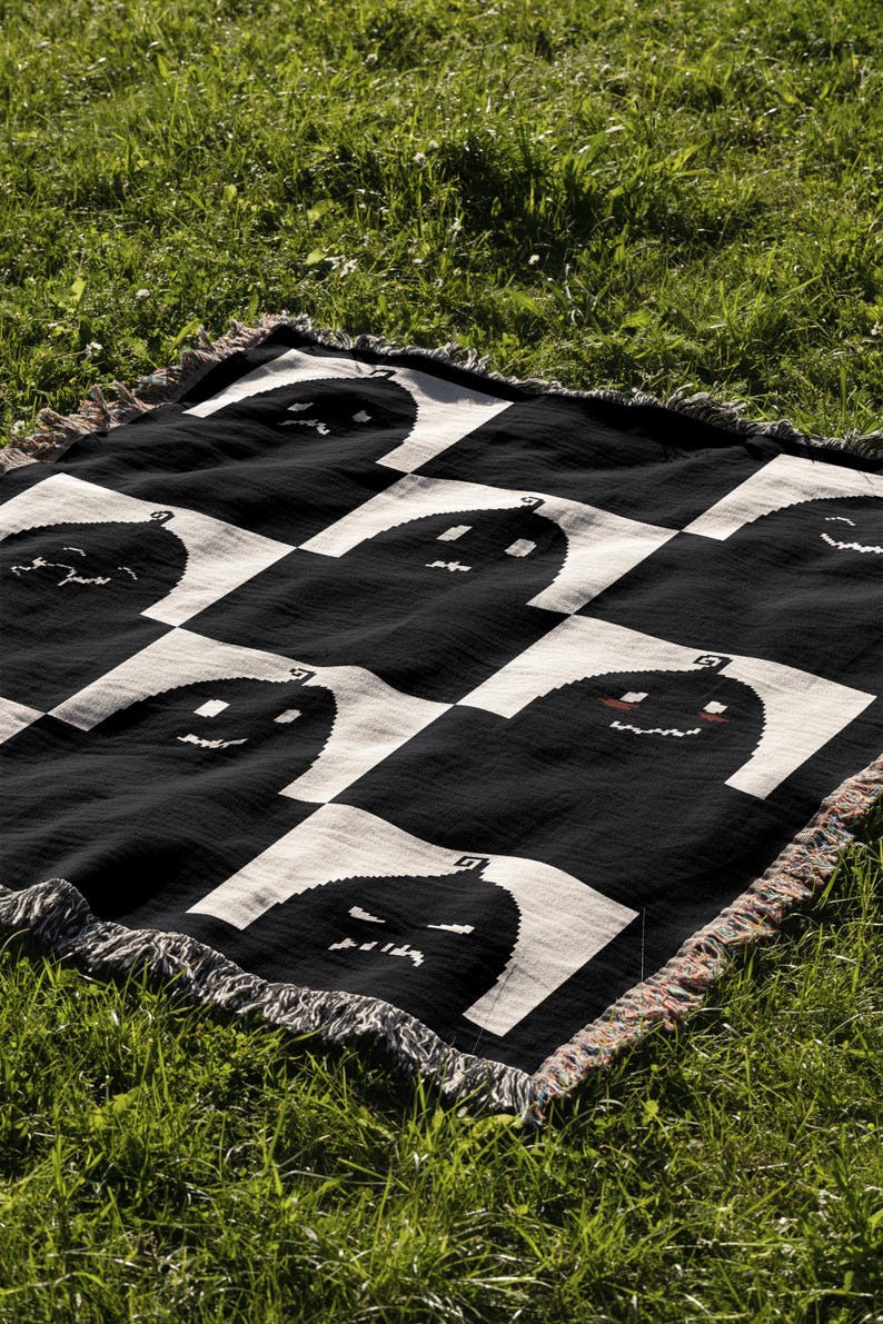 May include: Black and white checkered throw blanket with a pattern of smiling and frowning pumpkins. The blanket has a fringe border.