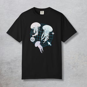 May include: Black t-shirt featuring a graphic design of three jellyfish in shades of white and blue. The jellyfish are set against a blue grid pattern with a star and a sphere. The shirt is a classic crew neck.