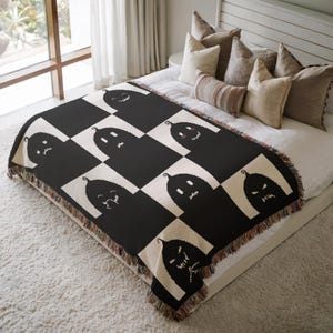 May include: Black and white woven throw blanket with a checkered pattern featuring a repeated design of black silhouettes of jack-o'-lanterns with different facial expressions.