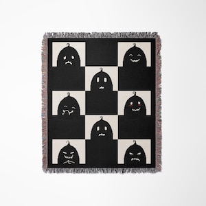 May include: A black and white checkered throw blanket with a pattern of nine black pumpkins with different facial expressions. The pumpkins are arranged in a 3x3 grid.