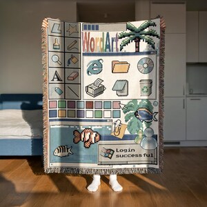 Peut inclure: Un plaid tiss&eacute; pr&eacute;sentant un design d'interface d'ordinateur nostalgique des ann&eacute;es 1990. Le motif comprend des ic&ocirc;nes pix&eacute;lis&eacute;es, un palmier, un poisson, un personnage trombone et une fen&ecirc;tre affichant le texte WordArt et Login successful.