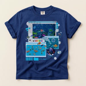 May include: Navy blue t-shirt featuring a retro computer-style graphic of an aquarium scene. The design includes fish, a dolphin, and the text "テクノロジー" in Japanese. The shirt is made of a soft material.