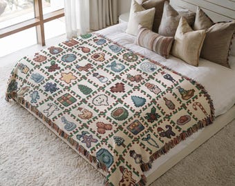 May include: A cream-colored throw blanket with a pixelated pattern of holiday-themed icons, including trees, gifts, and gingerbread men. The blanket has a fringed edge and is displayed on a bed with pillows.