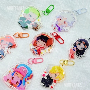 May include: Collection of anime character keychains. Each keychain features a different character in a chibi style, with vibrant colors and detailed designs. Keychains have various colored clasps, including green, pink, and gold. The brand name "Mintyartz" is visible.