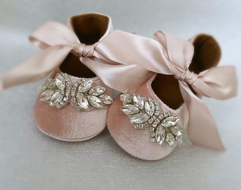Peut inclure: Une paire de chaussures de b&eacute;b&eacute; en velours rose avec un grand embellissement en strass et un n&oelig;ud en satin assorti.