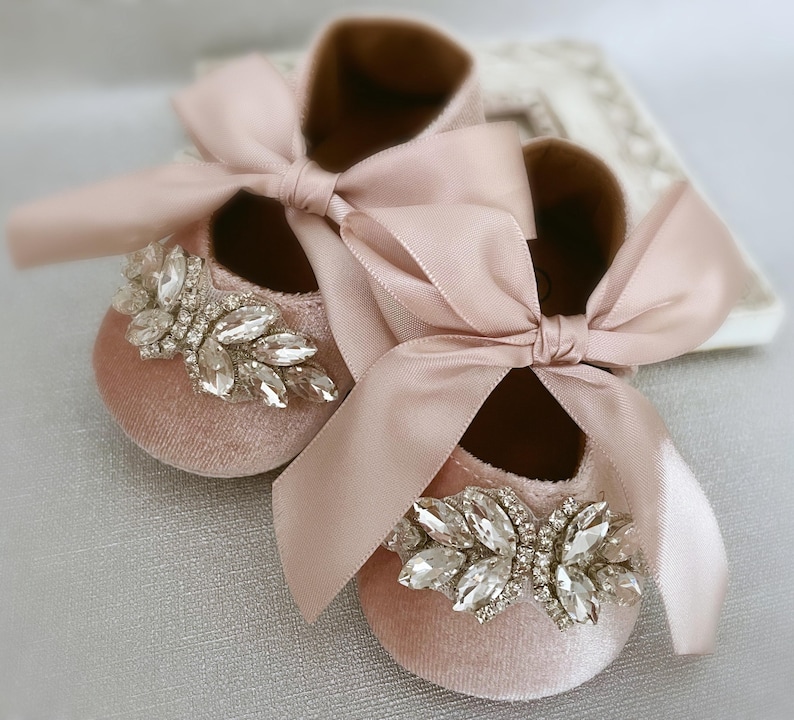 Peut inclure: Une paire de chaussures pour b&eacute;b&eacute; en velours rose avec un grand ornement en strass et un n&oelig;ud en satin rose assorti.
