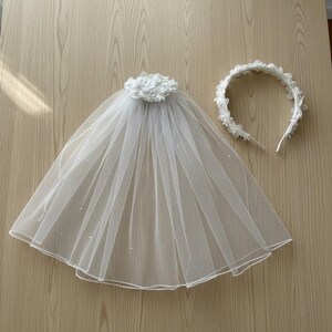 May include: A white bridal veil with a floral embellishment and a matching floral headband. The veil is made of sheer fabric and has a rounded shape. The headband is a simple band adorned with small white flowers.