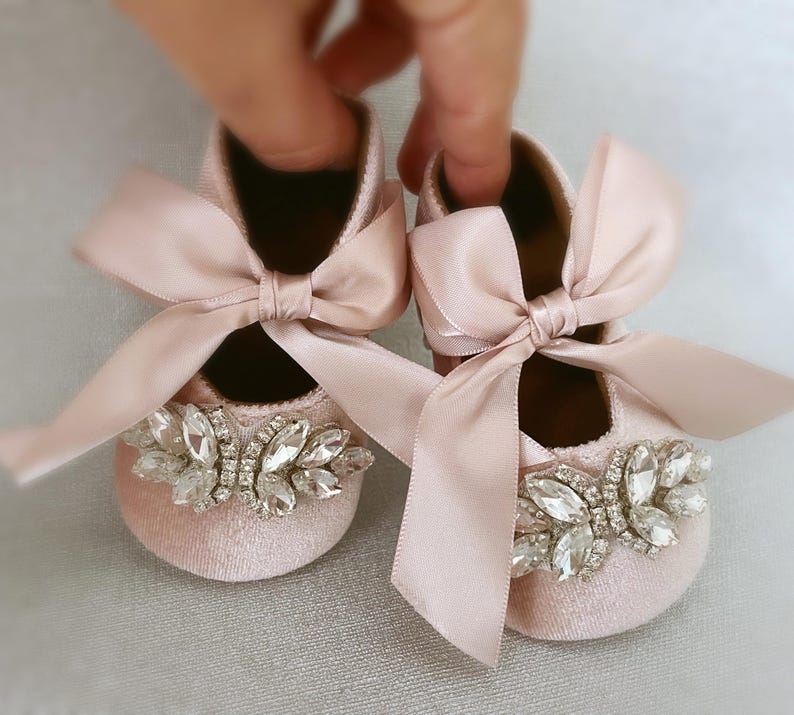 Peut inclure: Une paire de chaussures pour b&eacute;b&eacute; avec des n&oelig;uds en satin rose et des embellissements en cristal. Les chaussures sont faites d'un tissu rose doux et ont un design d&eacute;licat et f&eacute;minin.