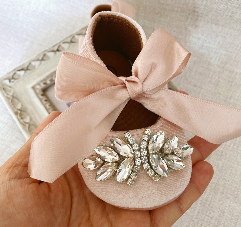 Peut inclure: Chaussures de b&eacute;b&eacute; en velours rose avec un grand embellissement en strass et un n&oelig;ud en satin assorti.