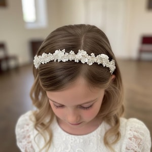 May include: A white floral headband with pearl accents. The headband features small, delicate white flowers and pearls, creating a refined and elegant look. This accessory is suitable for special occasions and celebrations.