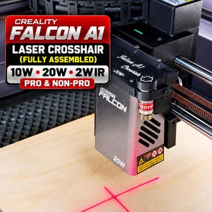Puede incluir: Un módulo láser Creality Falcon A1 con una proyección de retícula roja sobre una superficie de madera. La unidad cuenta con una etiqueta de 20W, una cadena portacables negra y pegatinas de advertencia. El texto dice Creality Falcon A1 Crosshair.