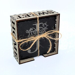 May include: A set of four black slate coasters with a personalized monogram and the name "JAMESON" in a decorative font. The coasters are packaged in a wooden box with the word "SWEET" cut out on the front.