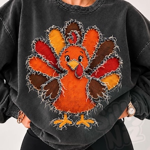 May include: A charcoal gray crewneck sweatshirt featuring a large, central applique of a turkey. The turkey is constructed from textured, frayed-edge fabric patches in shades of orange, red, yellow, and brown, with a prominent red wattle.
