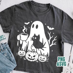 Pode incluir: Uma t-shirt cinzento-carv&atilde;o com uma impress&atilde;o gr&aacute;fica branca de um fantasma a segurar uma caneca de caf&eacute; a fumegar, um gato preto, tr&ecirc;s ab&oacute;boras, morcegos e estrelas. O texto PNG & SVG est&aacute; no canto inferior direito da imagem.