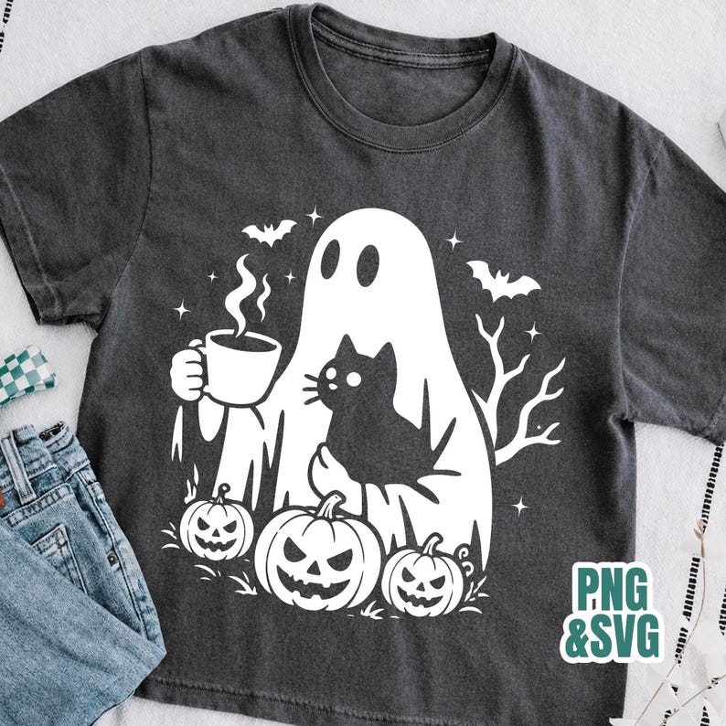 Pode incluir: Uma t-shirt cinzento-carv&atilde;o com uma impress&atilde;o gr&aacute;fica branca de um fantasma a segurar uma caneca de caf&eacute; a fumegar, um gato preto, tr&ecirc;s ab&oacute;boras, morcegos e estrelas. O texto PNG & SVG est&aacute; no canto inferior direito da imagem.