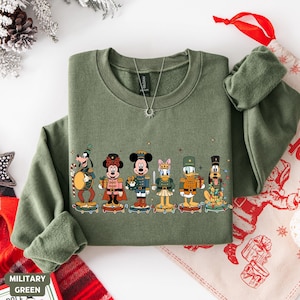 May include: Military green sweatshirt featuring a line of Disney characters dressed as toy soldiers. The characters include Mickey Mouse, Minnie Mouse, Donald Duck, and Goofy. The design is festive and holiday-themed.