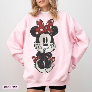 Puede incluir: Sudadera rosa claro con un gr&aacute;fico desgastado de Minnie Mouse. El personaje de dibujos animados est&aacute; en negro, blanco y rojo, con un lazo de lunares. El texto "LIGHT PINK" est&aacute; en la parte inferior de la imagen.
