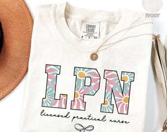 May include: A white t-shirt with a floral print design that spells out "LPN" for Licensed Practical Nurse. The shirt has a small bow at the bottom and the text "licensed practical nurse" underneath the floral design.